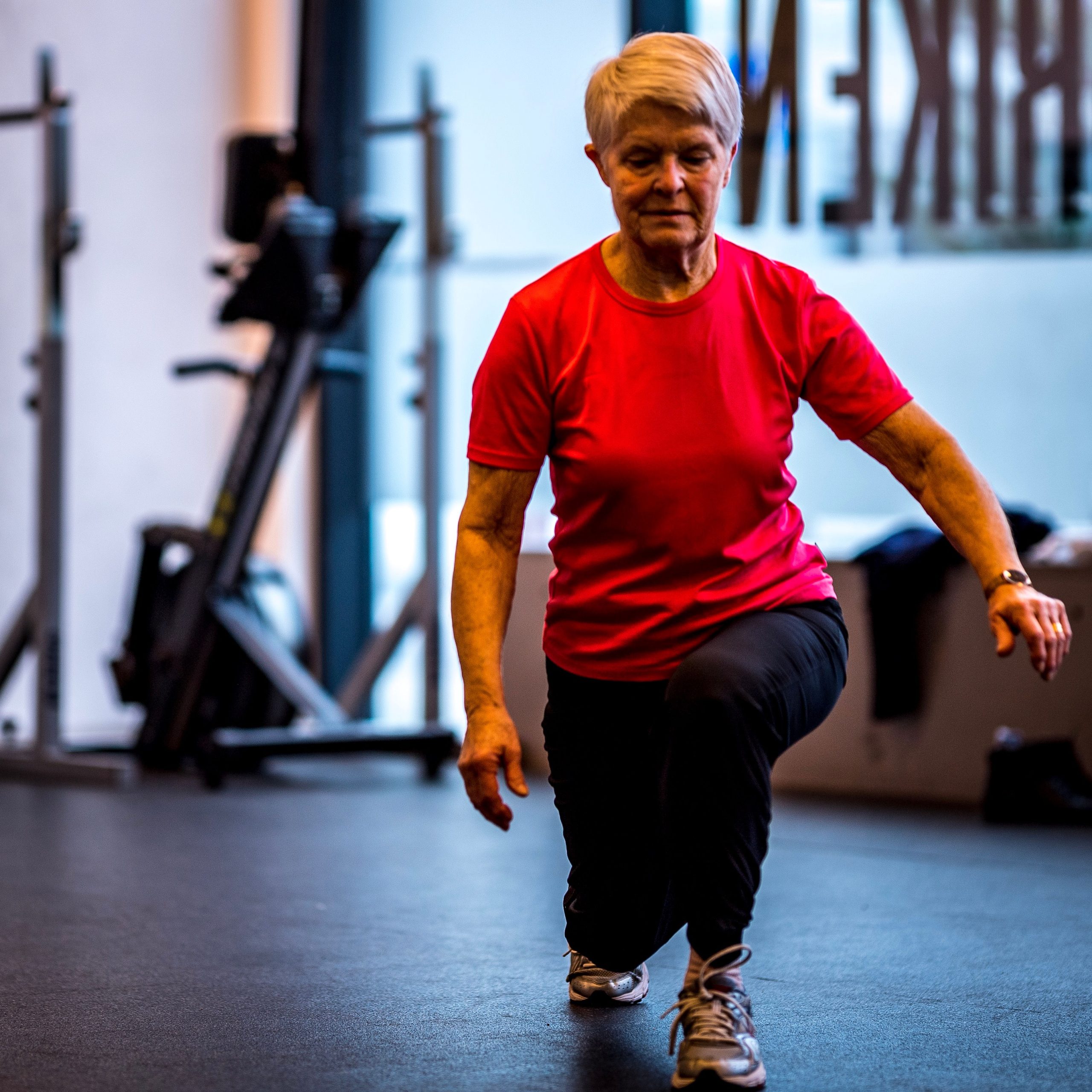 Äldre dam som gör utfallsteg i gymmet.